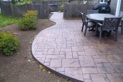 Curved stamped concrete patio beside a fenced yard with outdoor table and chairs