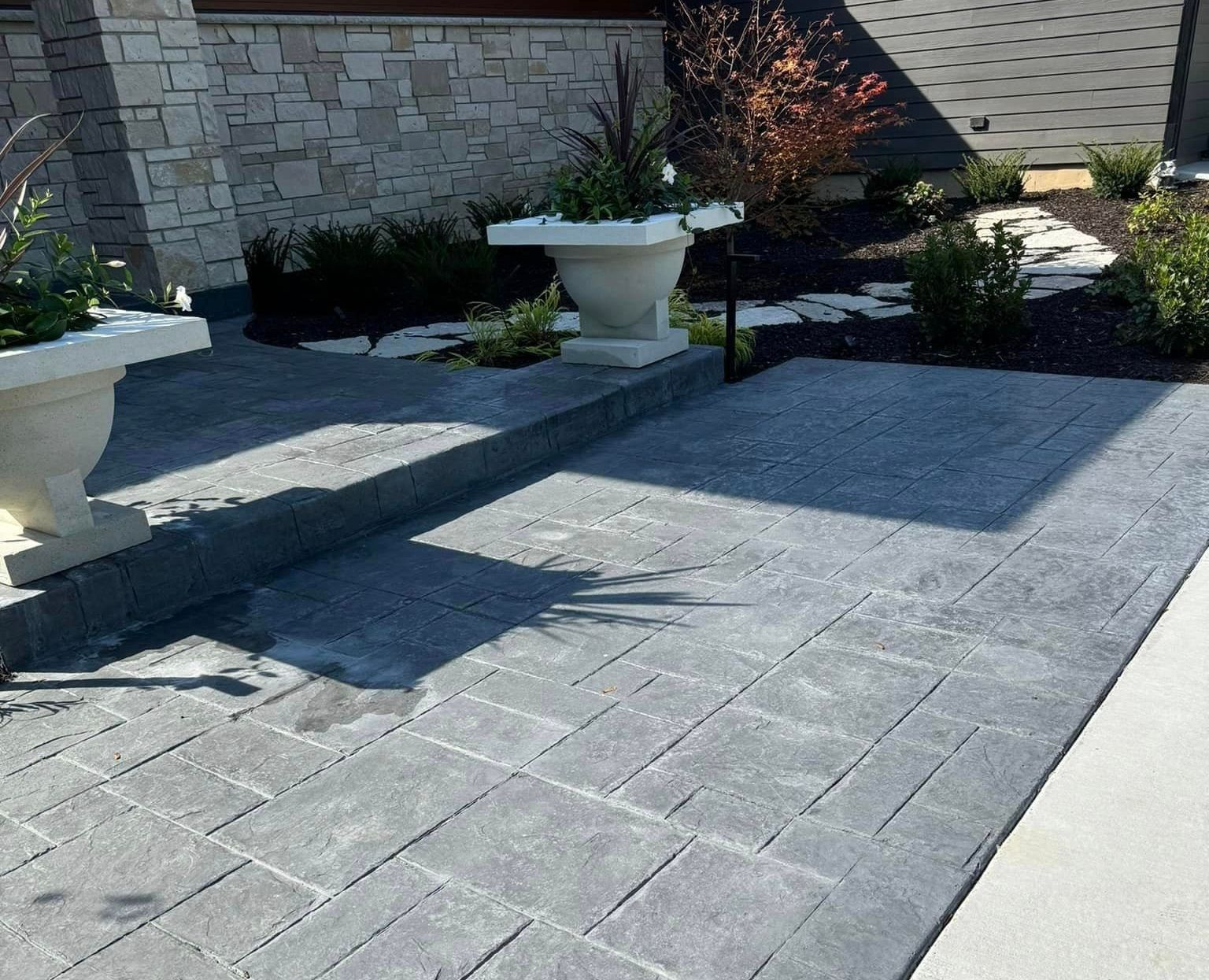 Stone patio beside a garden wall with potted plants and a sunlit paver walkway