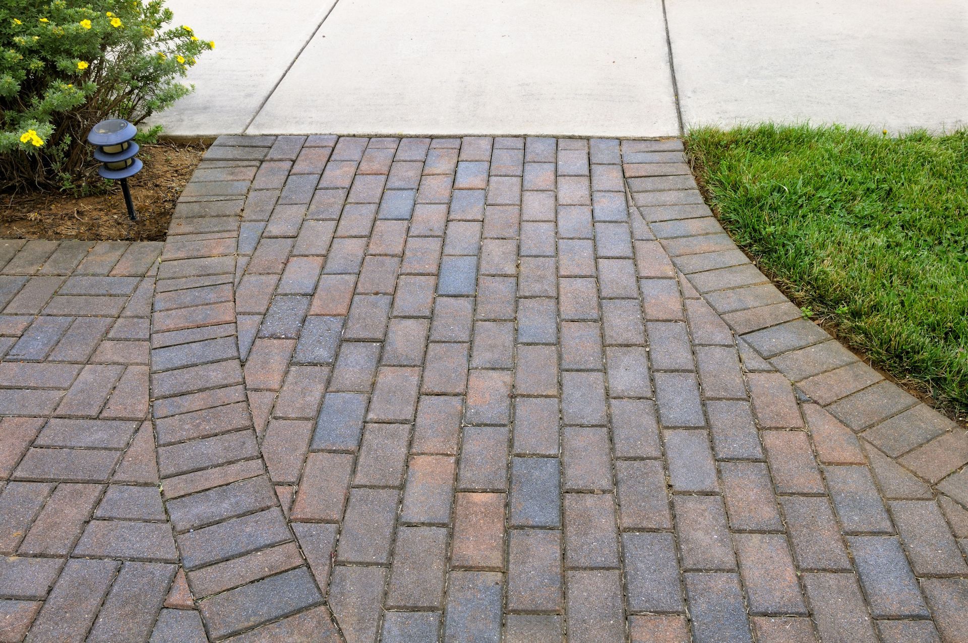 Curved brick pathway bordered by grass and pavement in a yard