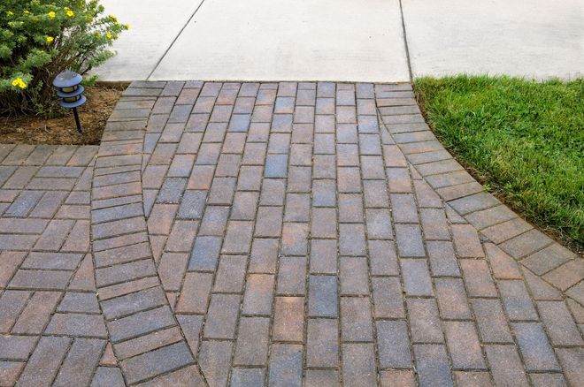 Curved brick pathway bordered by grass and pavement in a yard