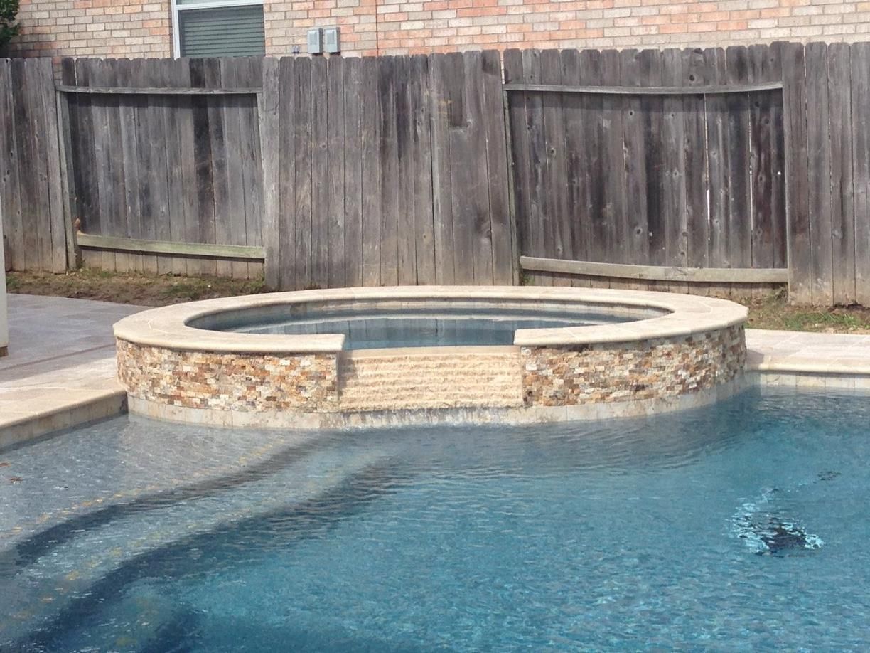 Pool with built-in hot tub; stone and wood fence in background; blue water.