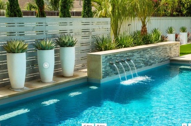 Swimming pool with waterfall feature and large white planters with green plants.