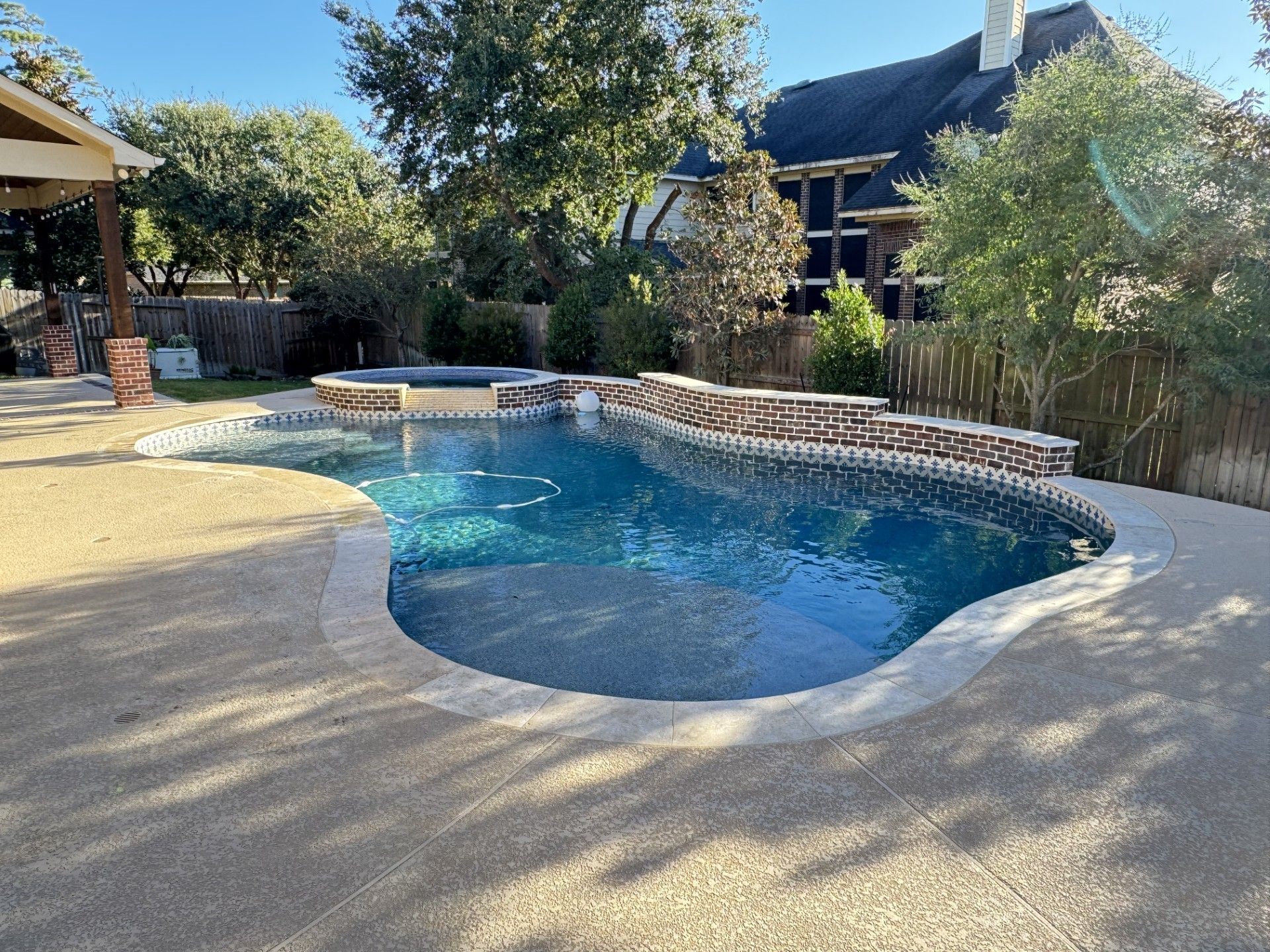 Swimming pool with waterfall feature and surrounding concrete patio on a sunny day.