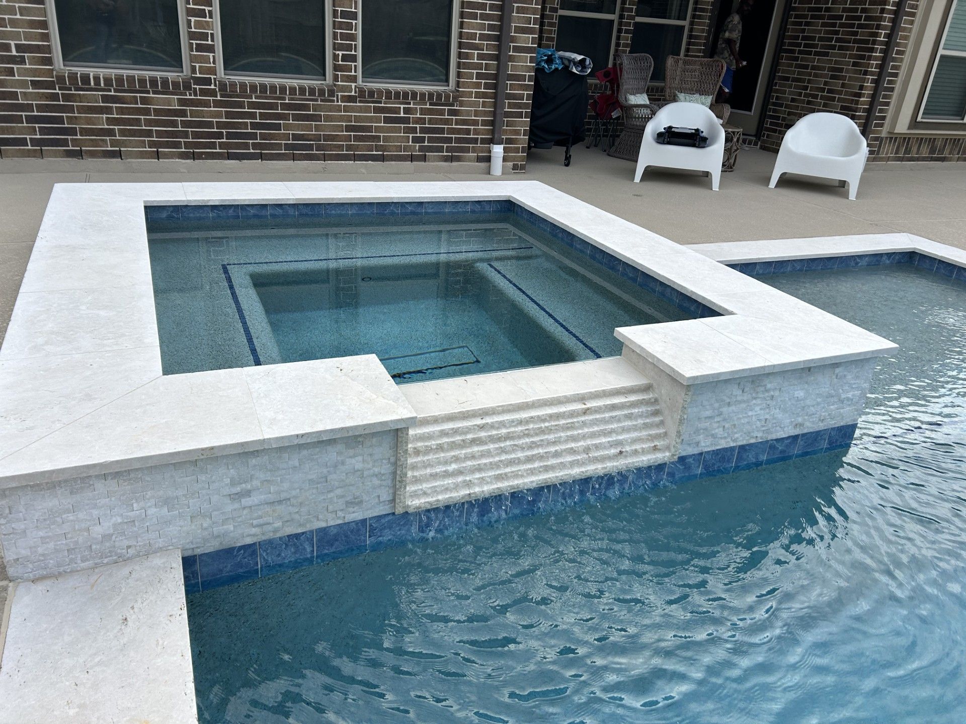 Pool with raised hot tub, blue water, white coping, steps. Backyard setting.