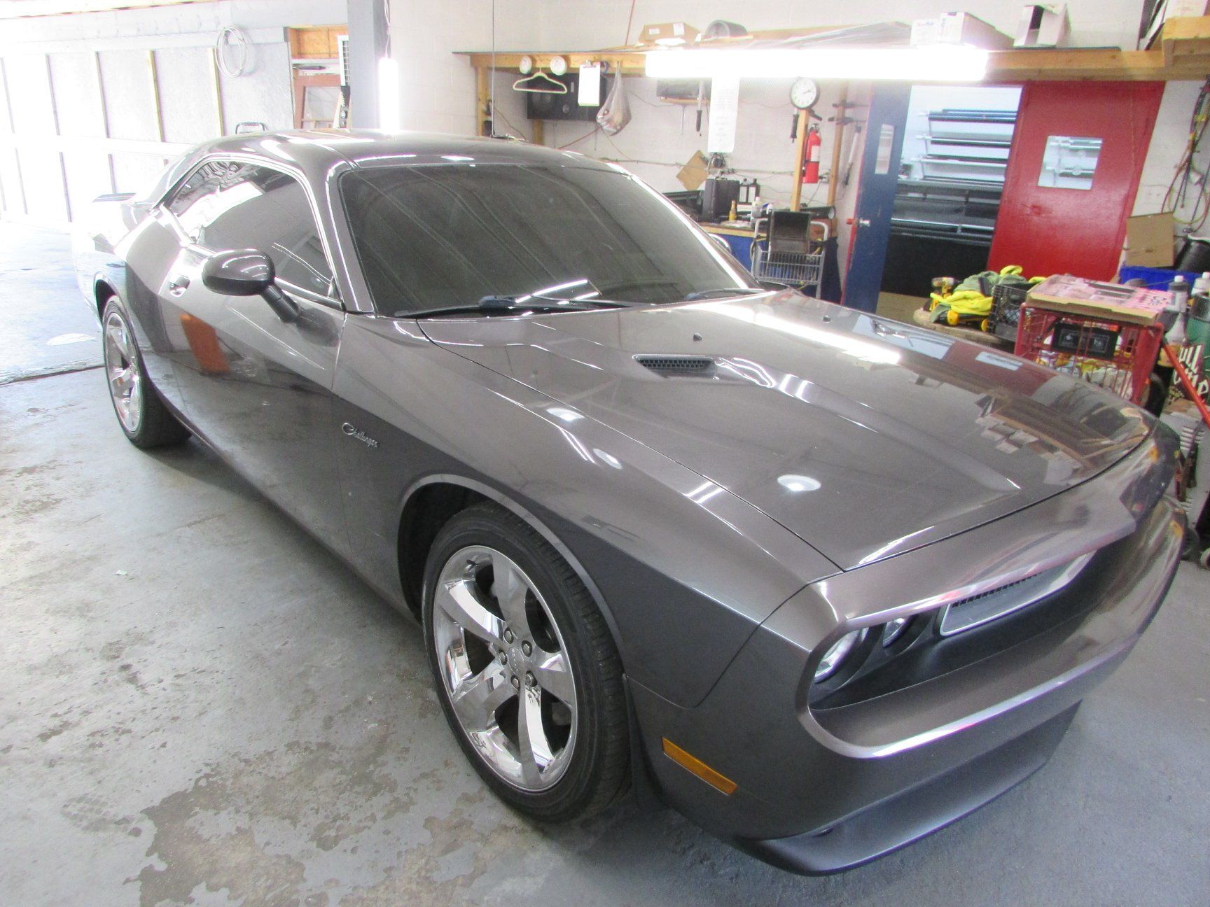 A gray dodge challenger is parked in a garage.