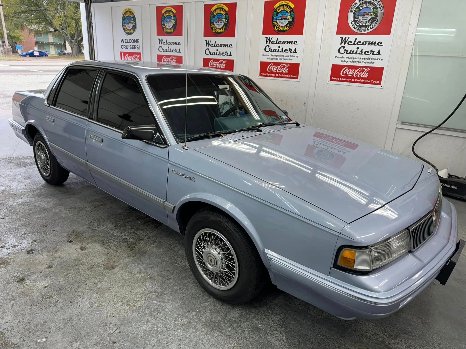 A blue car is parked in front of a coca cola sign