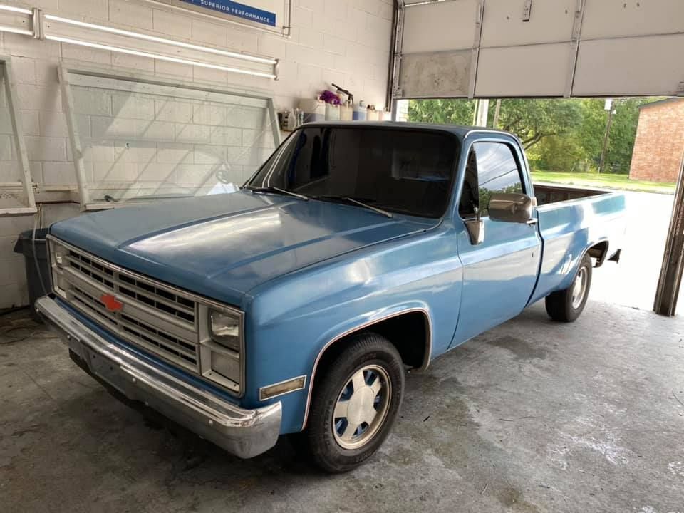 A blue truck is parked in a garage next to a garage door.