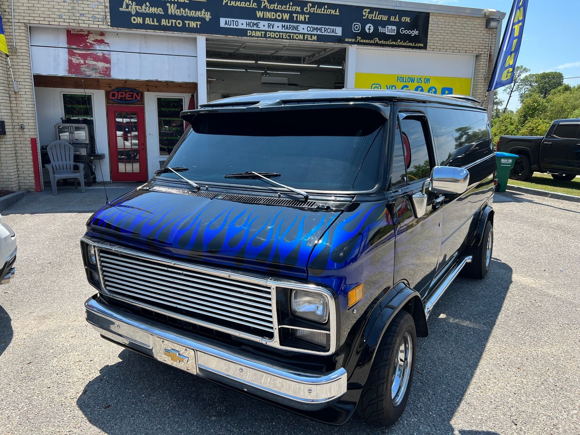 A blue van is parked in front of a car dealership.
