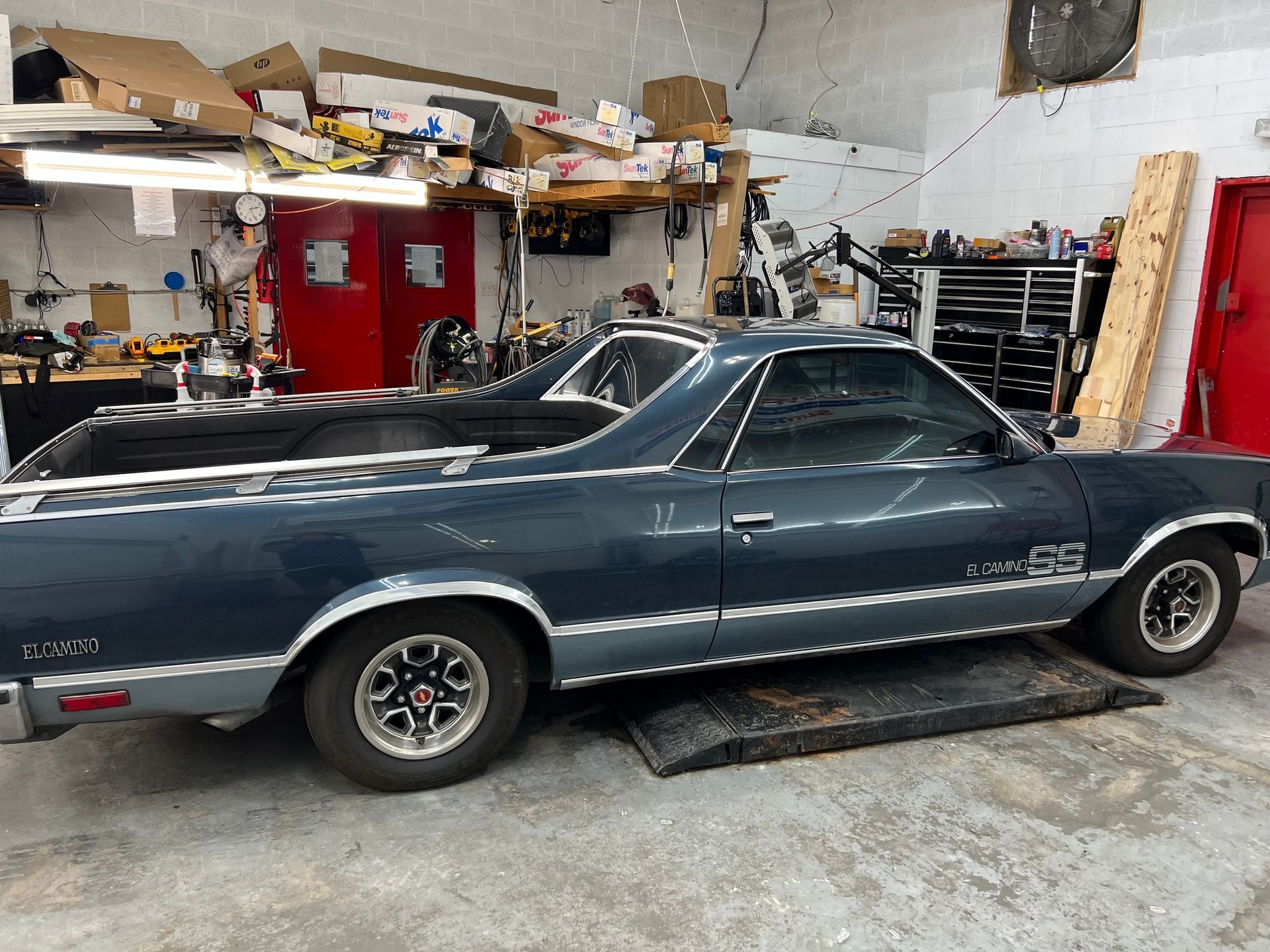 A blue el camino truck is parked in a garage.
