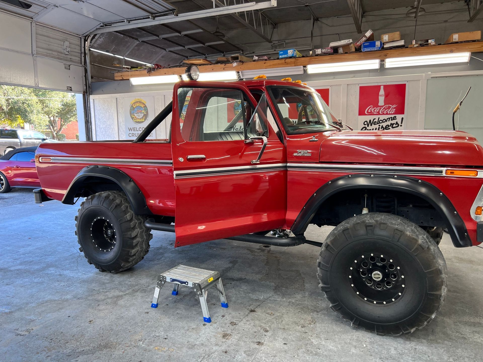 A red truck is parked in a garage with the door open.