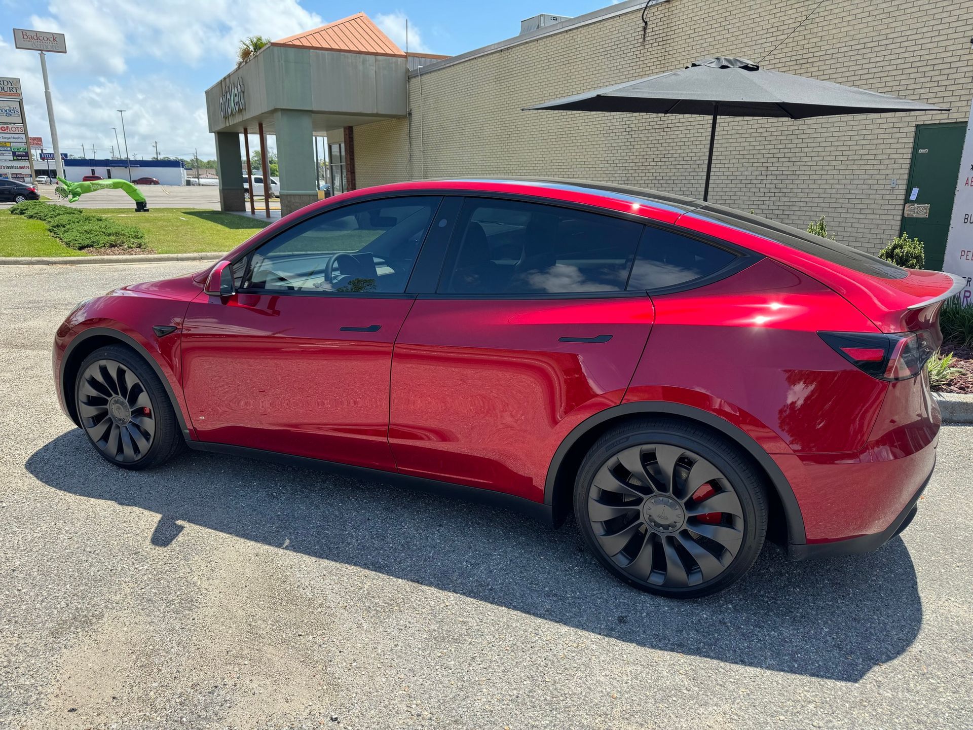 A red tesla model y is parked in a parking lot in front of a building.