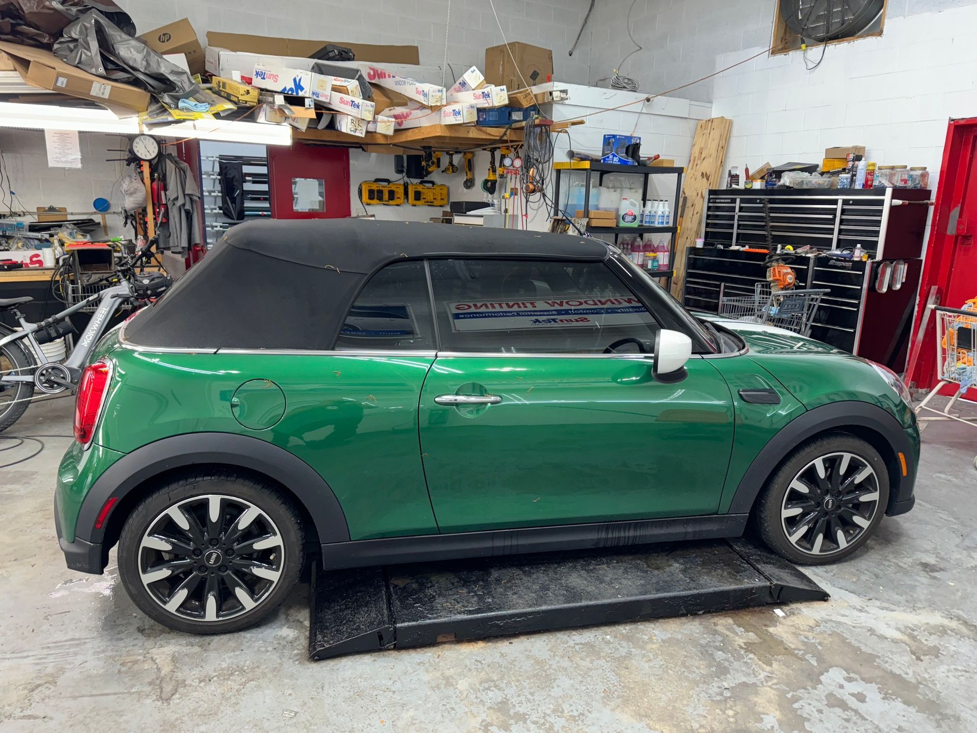 A green mini cooper convertible is parked in a garage.