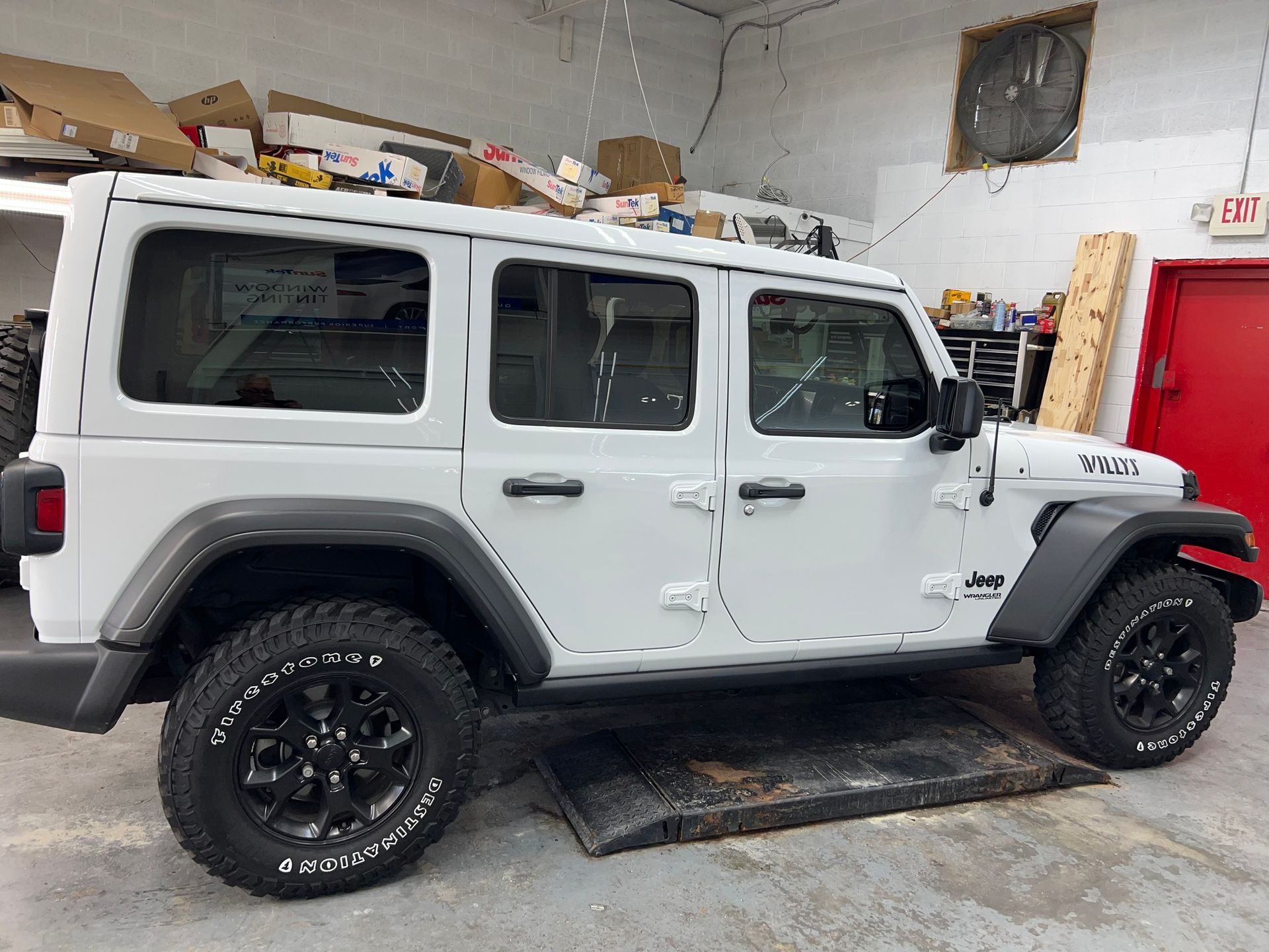 A white jeep is parked in a garage next to a red door.