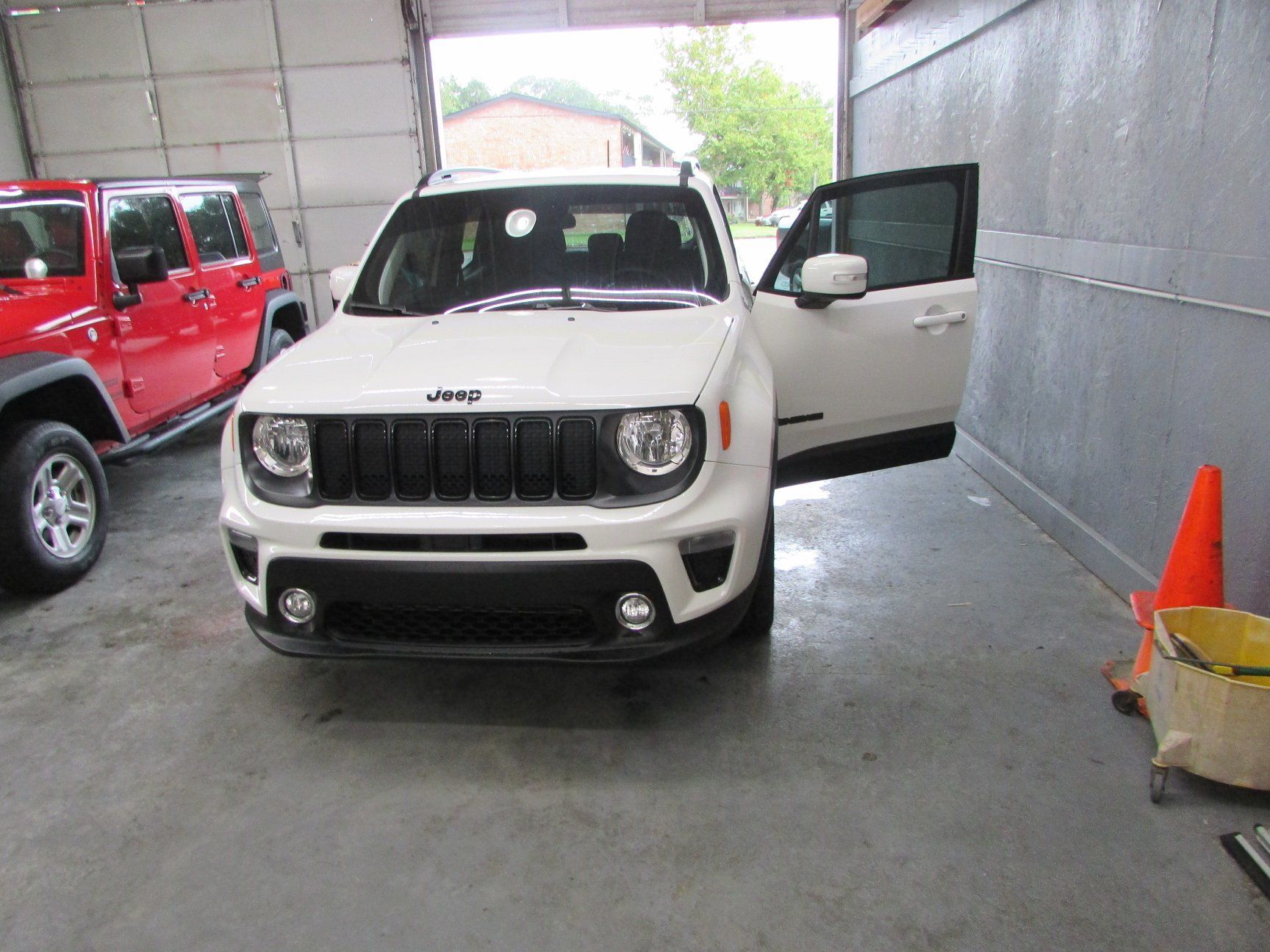 A white jeep renegade is parked in a garage with its doors open.