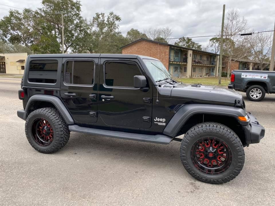A black jeep wrangler with red wheels is parked on the side of the road.