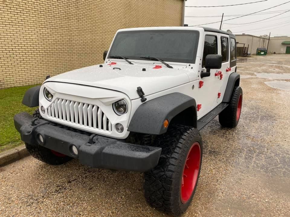 A white jeep with red wheels is parked in front of a brick building.