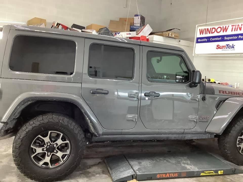 A gray jeep is parked on a lift in a garage.