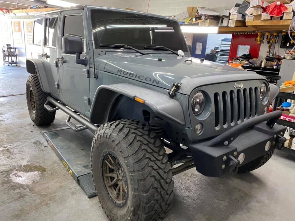 A jeep wrangler is parked on a lift in a garage.