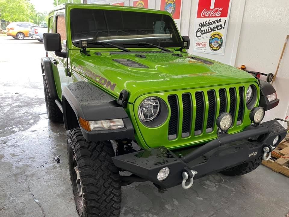 A green jeep is parked in front of a coca cola sign.