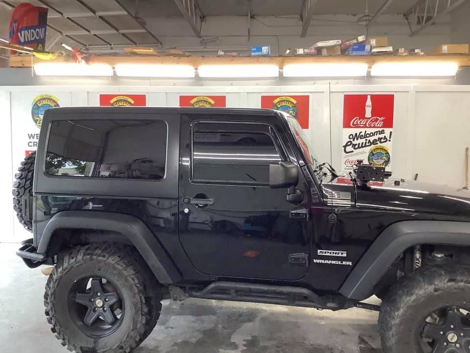 A black jeep is parked in front of a coca cola sign