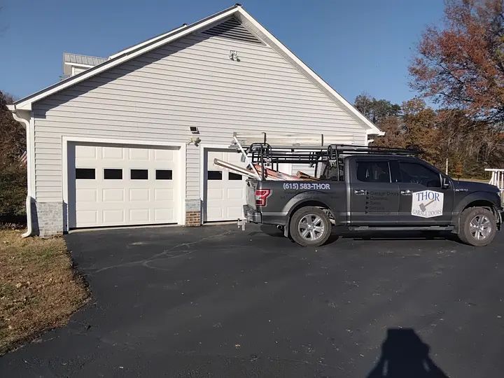 Two-car garage with white doors, gray siding, and a parked truck with equipment.