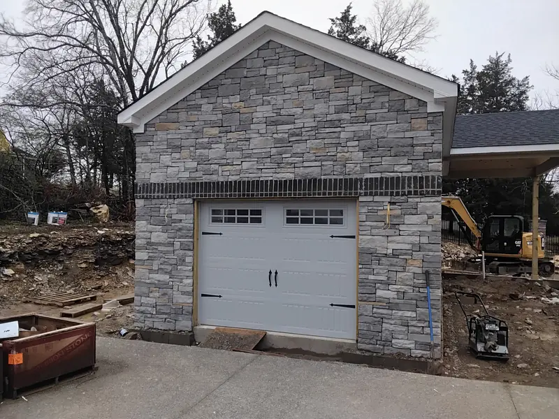 Stone-covered garage with white door, construction site. Gray stonework, white trim.
