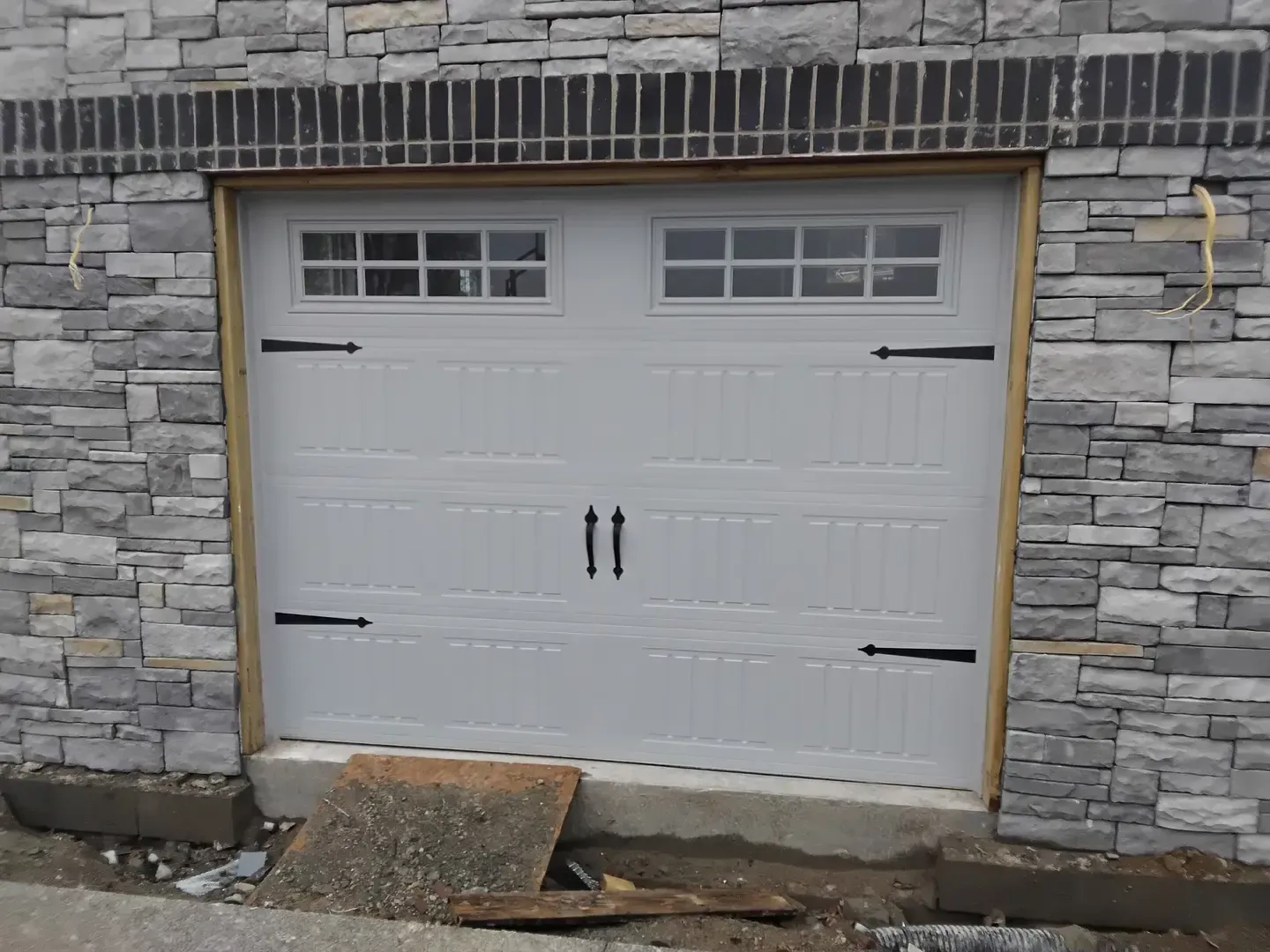 White garage door with windows, black hardware, set in stone facade.