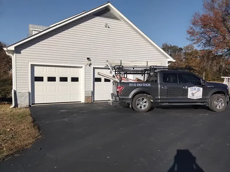 Garage with two white doors, gray siding, and a dark pickup truck parked in front.