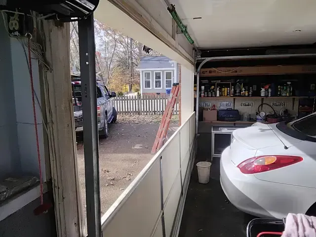 Garage door open, showing a car inside and a view of the outside yard with a vehicle and fence.
