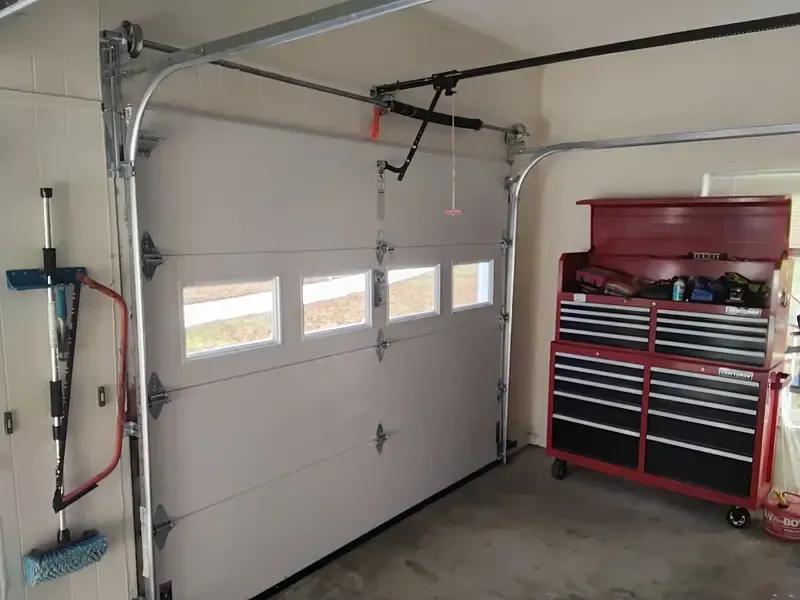 White garage door, partially open, with windows. Garage interior with red tool chest and cleaning tools.