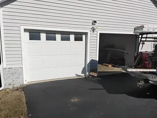 White garage doors on a light-colored house; one door closed, one open showing interior. Asphalt driveway.