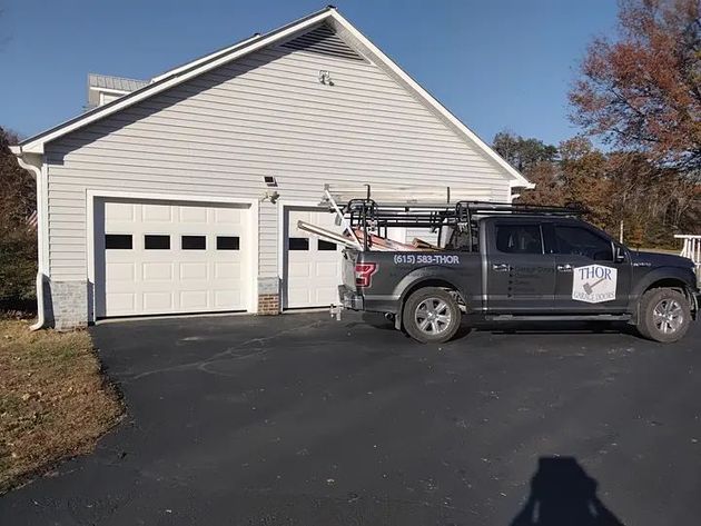 Gray truck parked in front of a light gray garage with two white garage doors; blue sky.