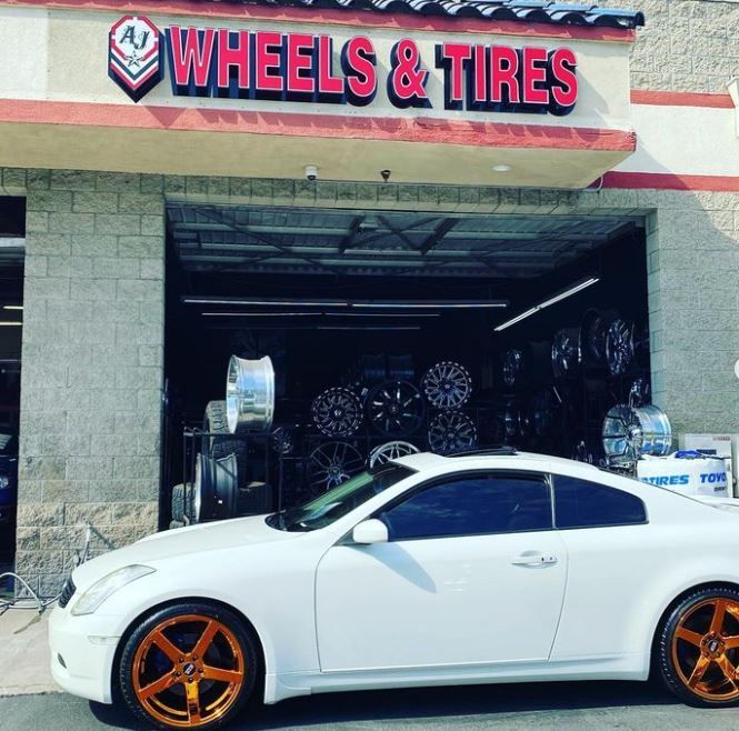 A white car is parked in front of A J Wheels & Tires