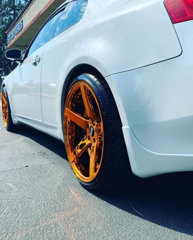 A white car with gold wheels is parked in front of a tire shop