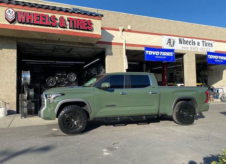 A green truck is parked in front of a wheels and tires store
