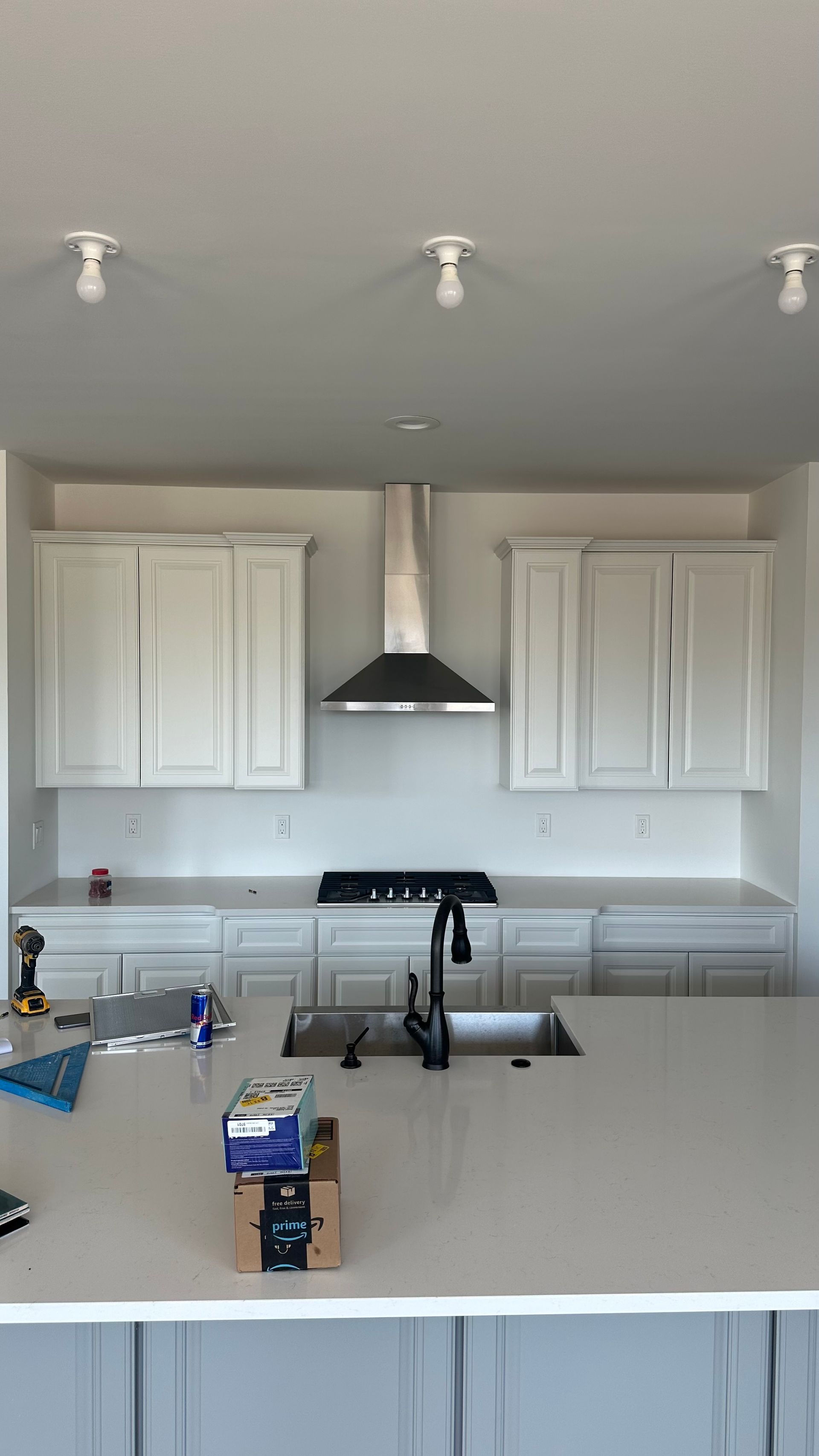A kitchen with white cabinets, a sink, a stove and a hood.