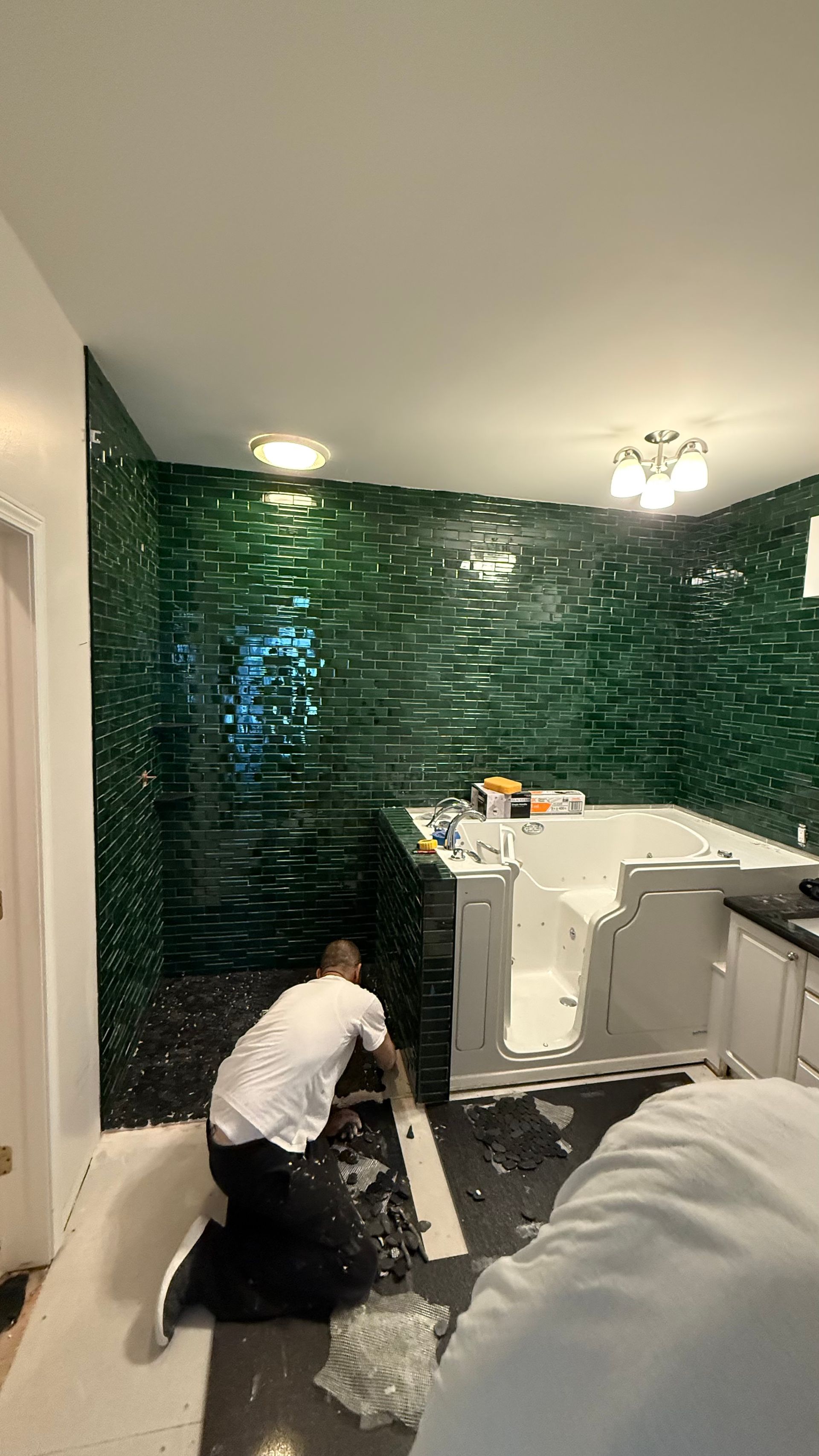 A man is kneeling down in a bathroom with green tiles.