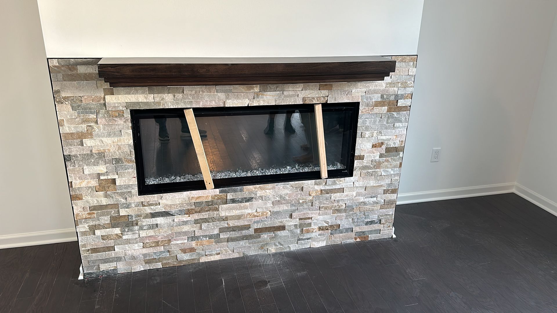 A fireplace with a stone wall and a wooden mantle in a living room.