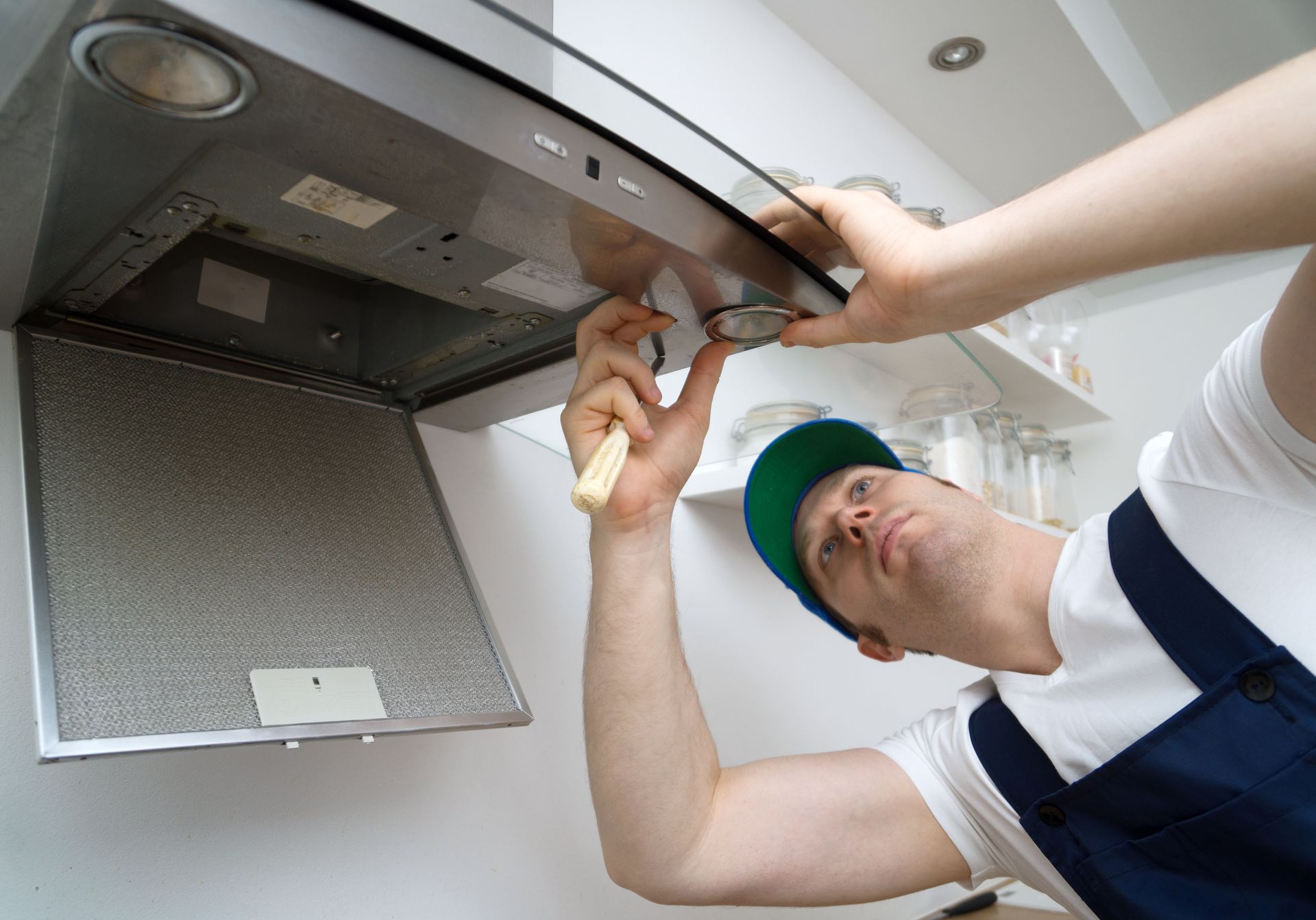 Man in work clothes repairing kitchen range hood.
