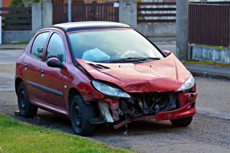 Red car severely damaged in a collision, parked on the side of a street.