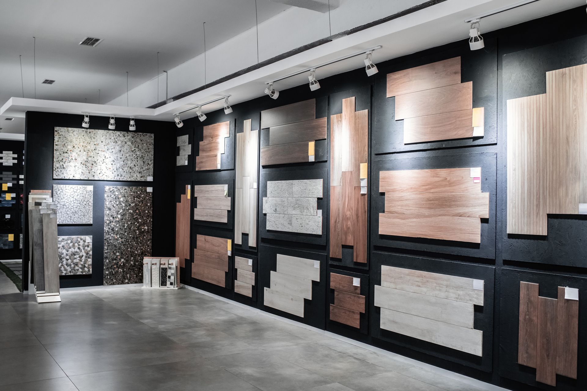 Modern showroom wall displaying assorted tile and stone samples in black, gray, and wood tones.