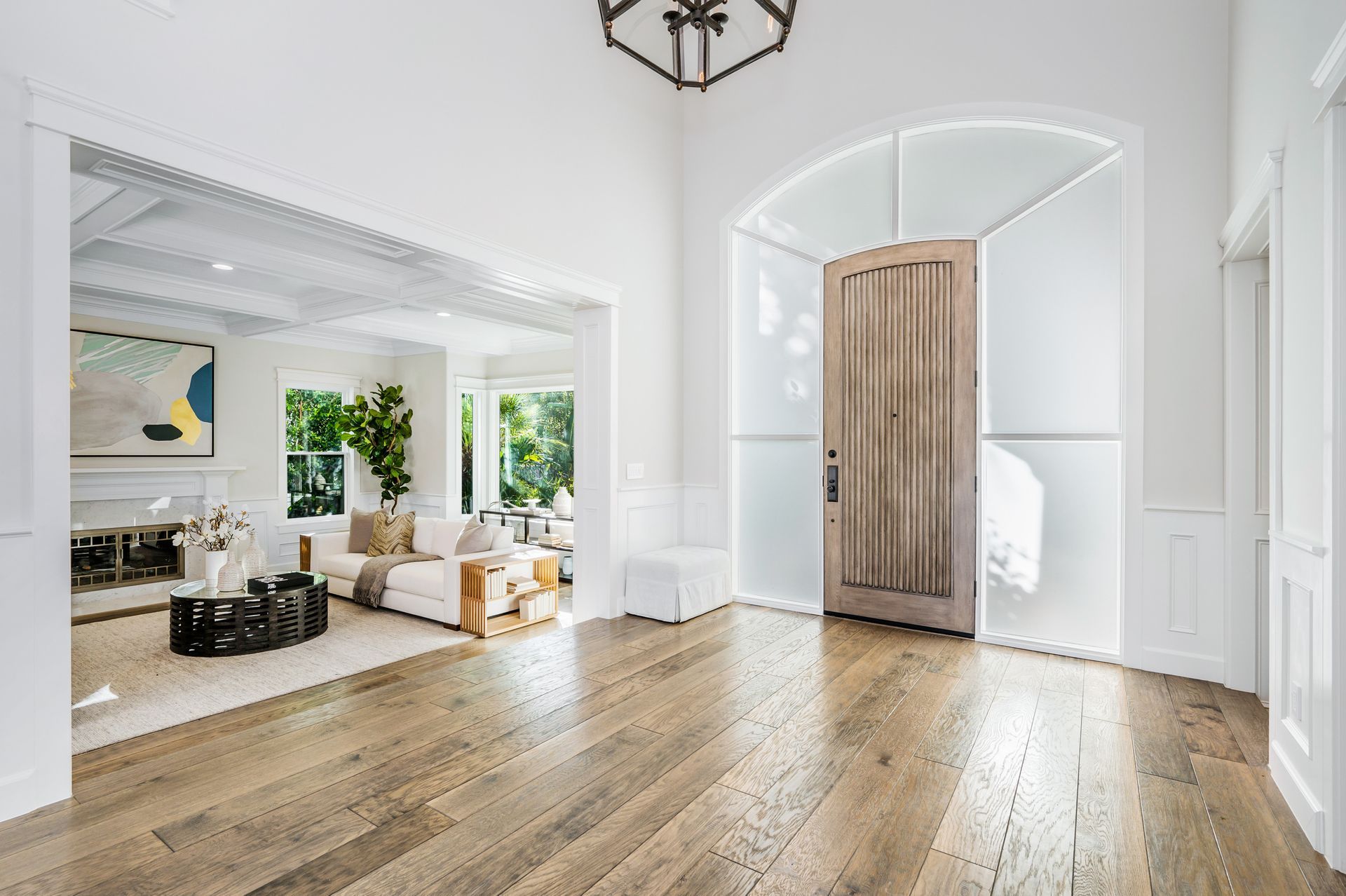 Bright foyer with wood floors, arched doorway, and rustic barn-style door leading to a sunlit living room.