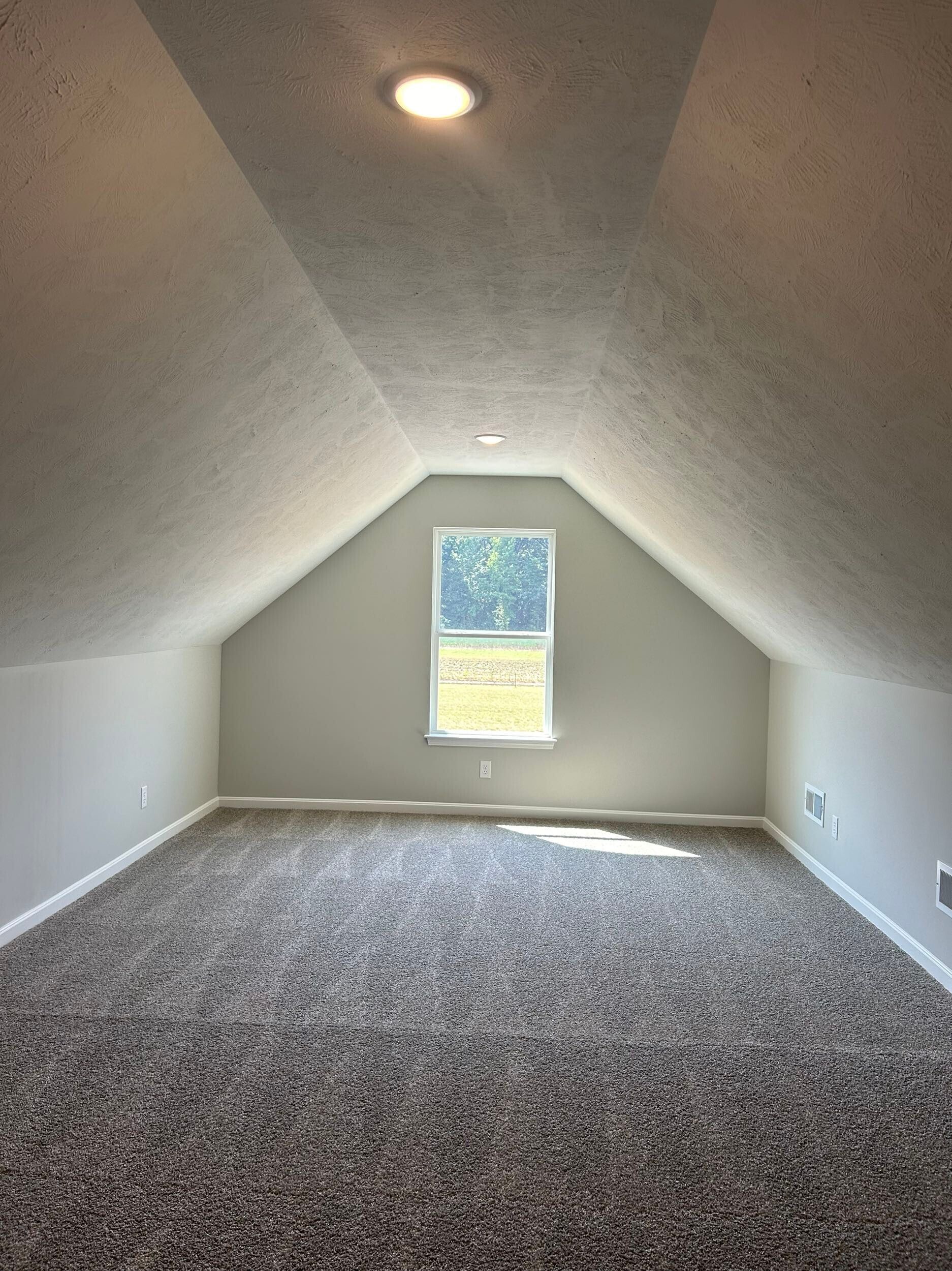Empty carpeted attic room with sloped ceiling and a small central window.
