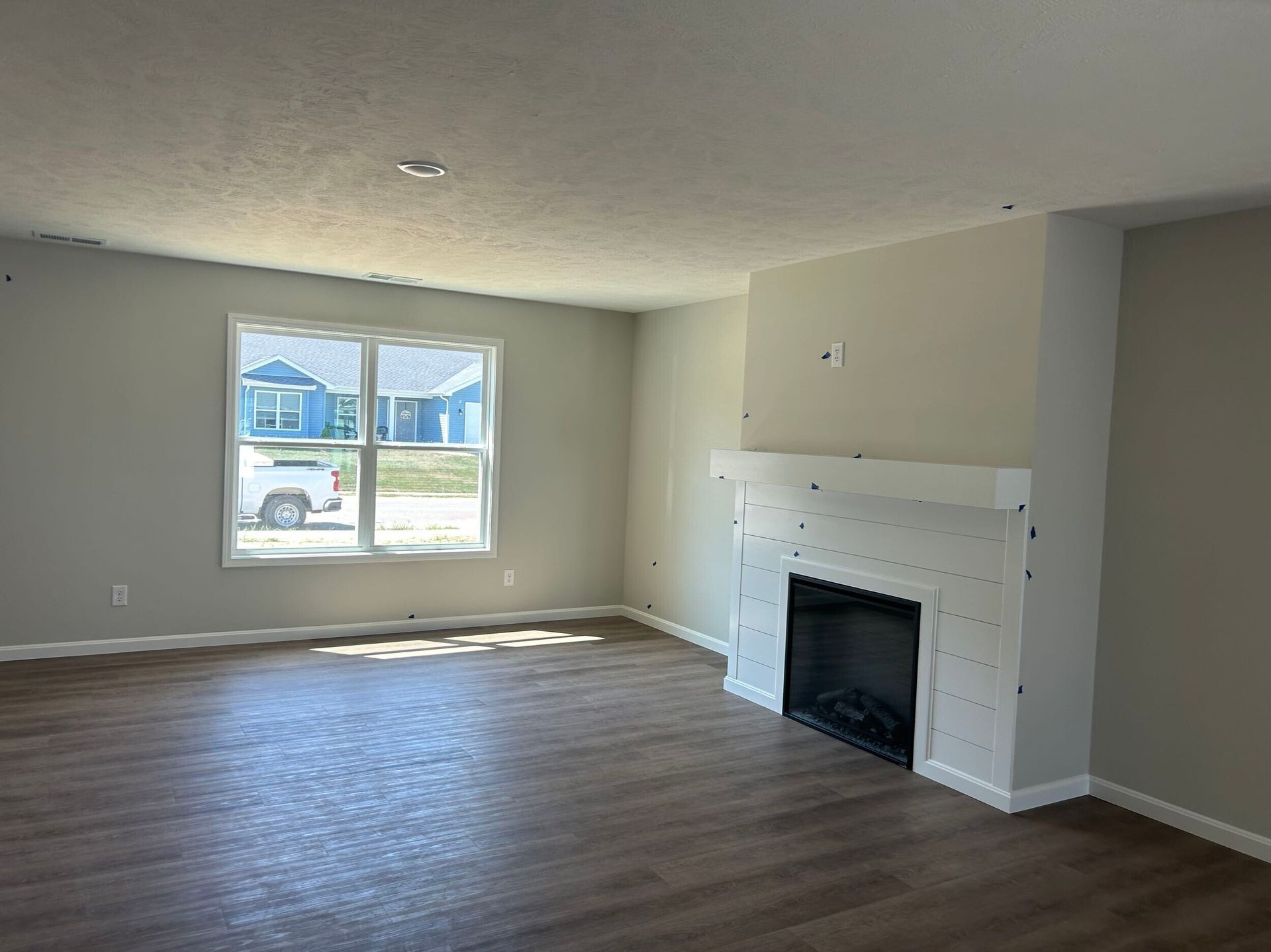 Empty living room with gray walls, wood floor, window light, and a white fireplace mantel.