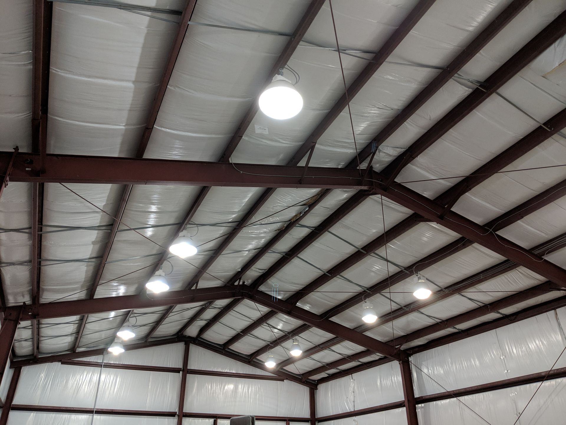 Interior view of a metal building with exposed beams, insulation, and bright overhead lights.
