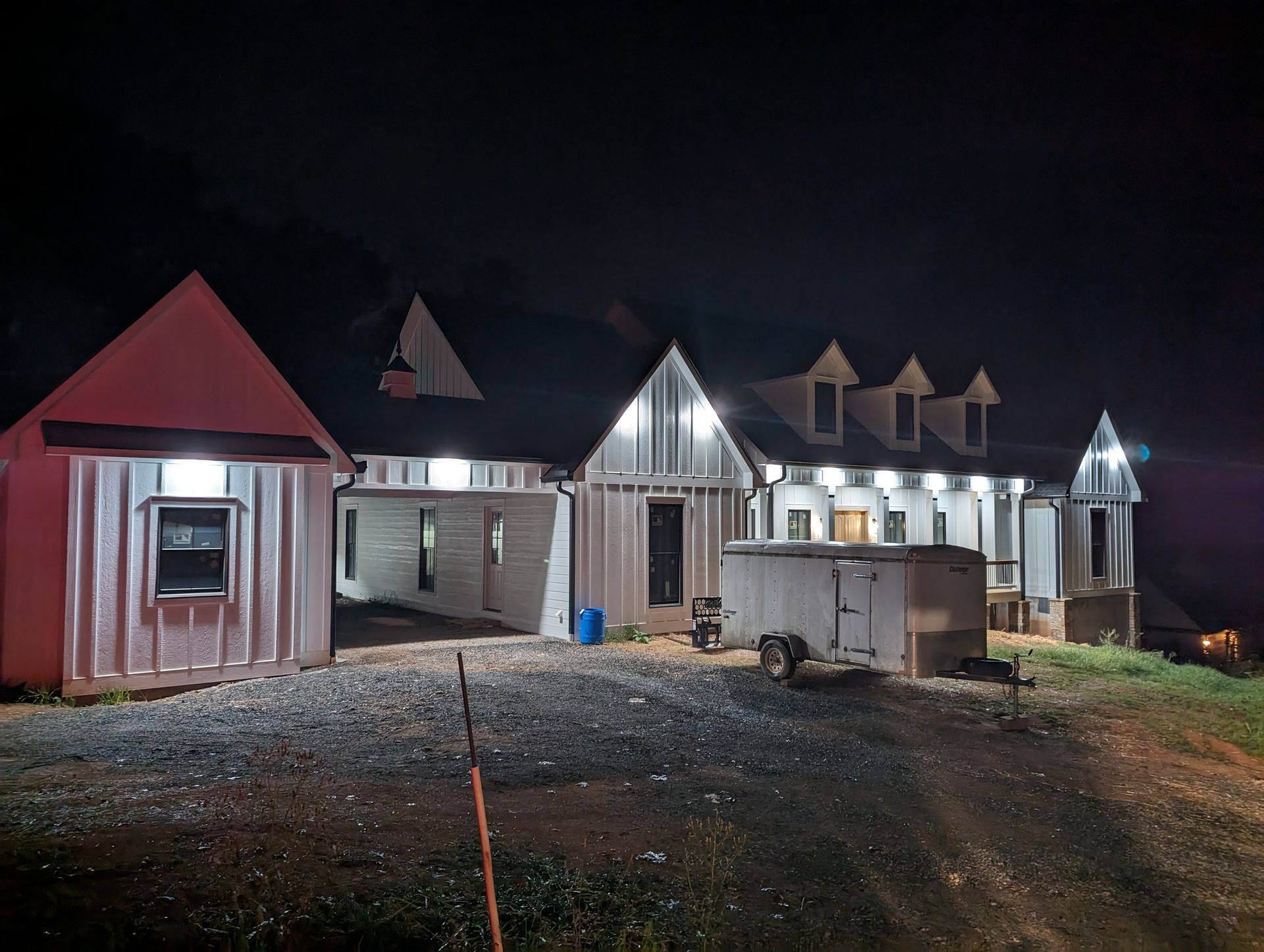 Night view of a partially constructed white house with bright exterior lights. Trailer parked outside.