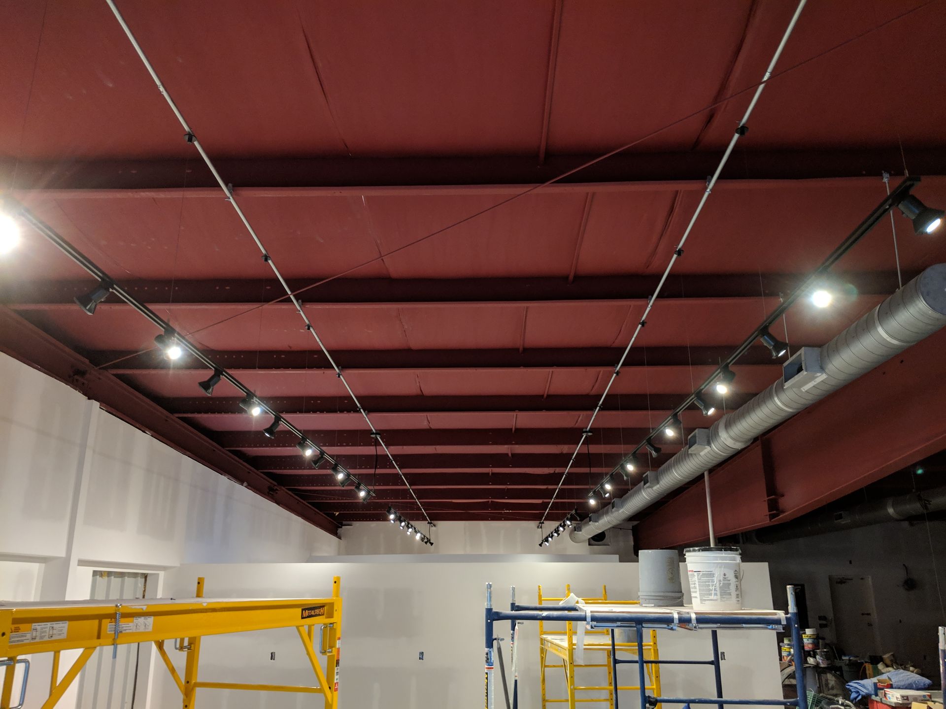 Red ceiling with track lighting and exposed beams; scaffolding below.