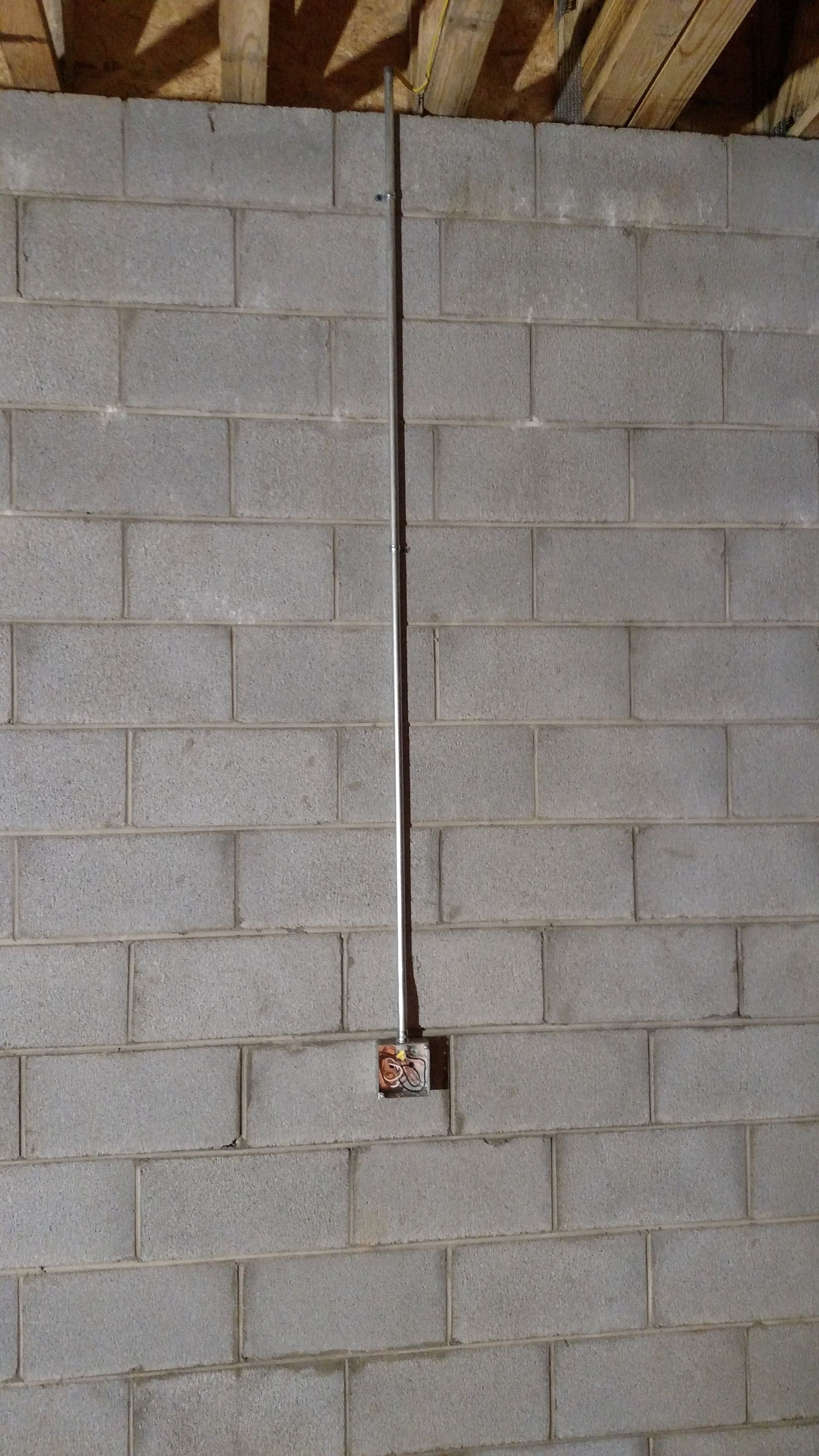 A metal conduit runs vertically on a gray cinder block wall to a square outlet box near the bottom.