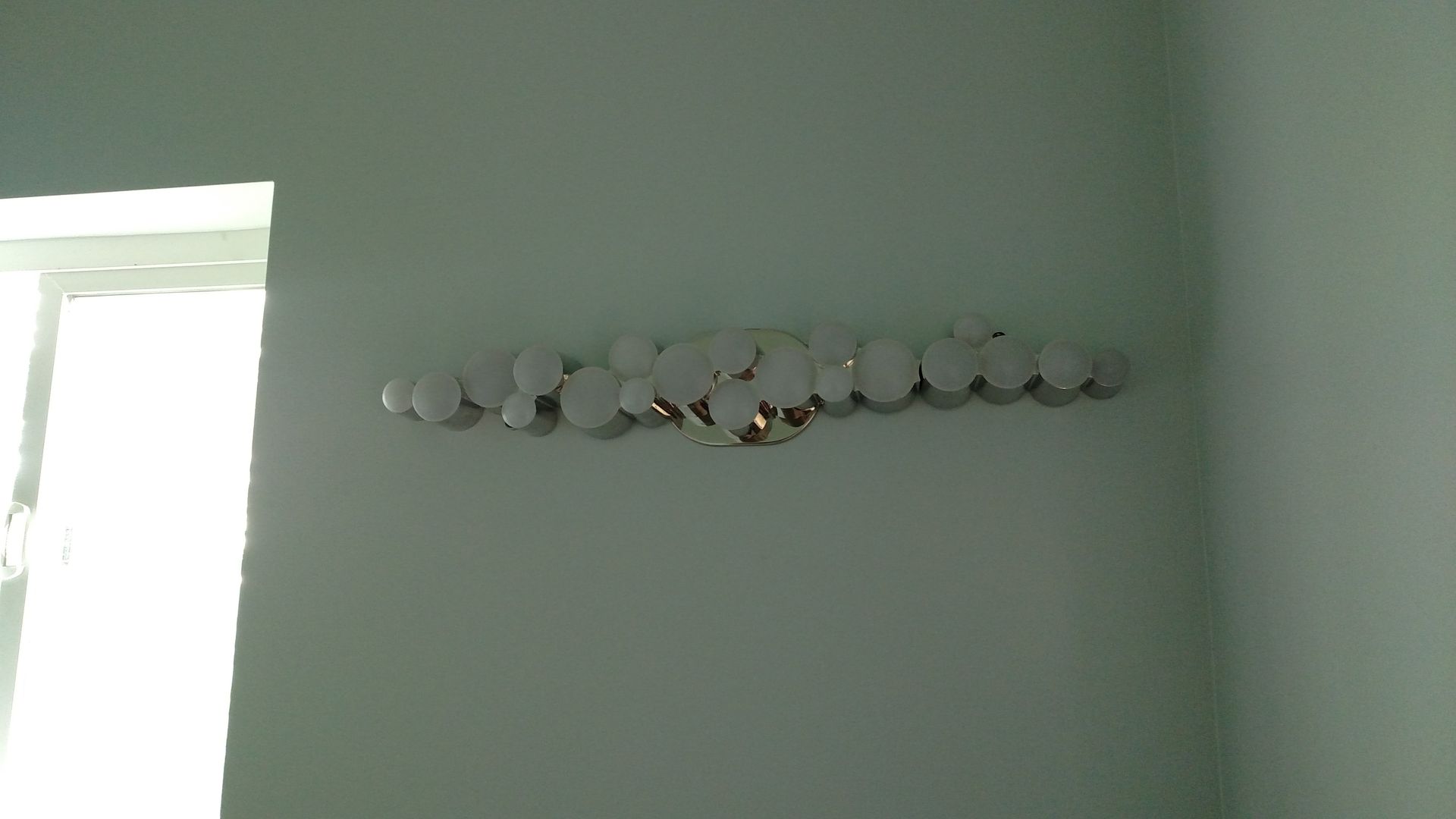A long, silver light fixture with many circular bulbs is mounted on a light green wall.
