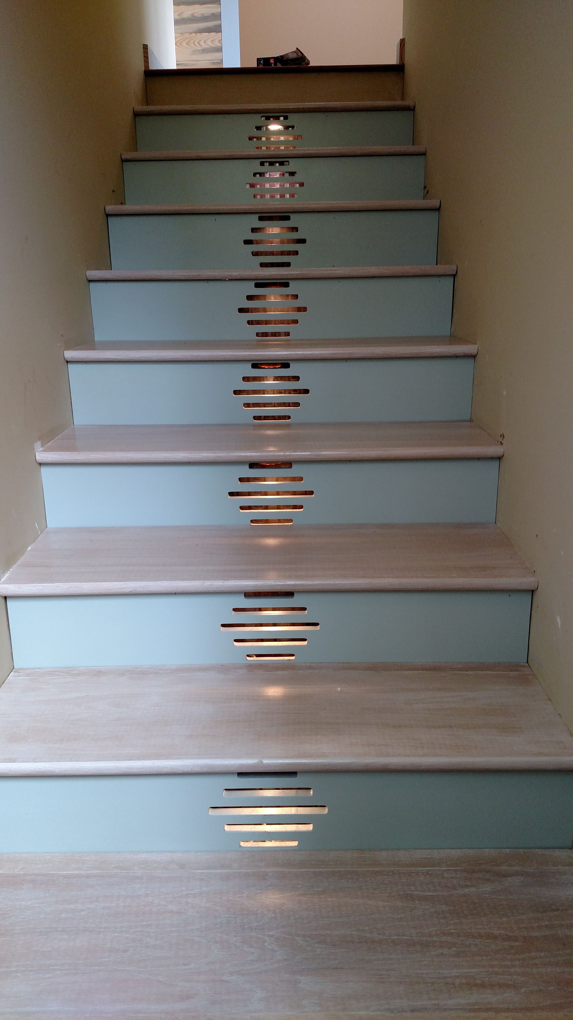 Staircase with light blue risers and light-colored steps. Decorative horizontal light fixtures are set in the risers.